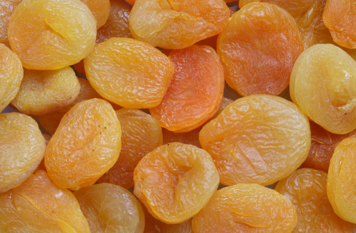 Dried apricots in a wooden bowl on a white wooden background. The concept of dried fruits. Healthy sweets.