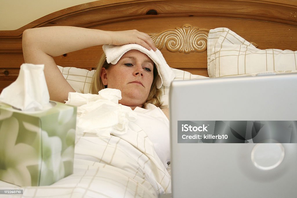 A woman sick in bed using a laptop A woman is sick in bed Adult Stock Photo