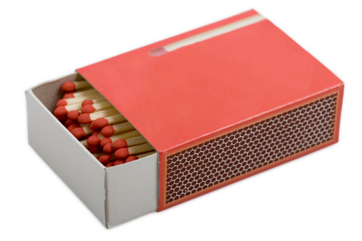 Close up of open cardboard match box filled with wooden matches with red match heads on white background