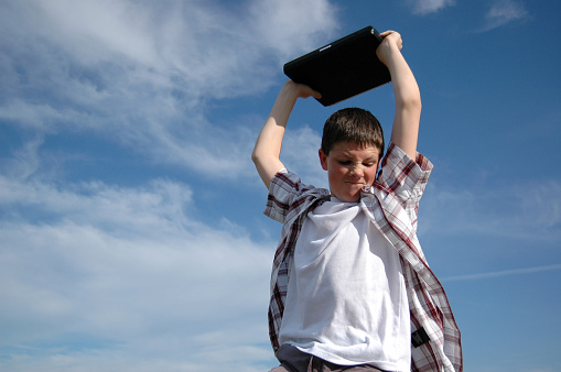 Angry, frustrated adolescent boy with laptop held over his head ready to be thrown to the ground. Pressure to succeed faced by our children today.