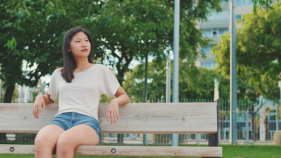 Beautiful brunette girl is enjoys relaxing while sitting on bench in city park