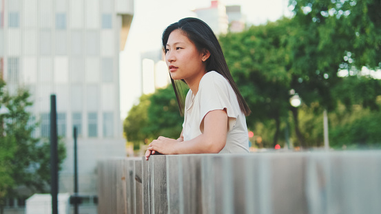 Young thoughtful woman stands leaning on railing and looks into the distance