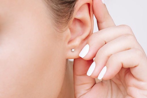 Ear piercing. Cropped shot of a young woman wearing elegant stud earrings. Jewelry with gemstones, accessories