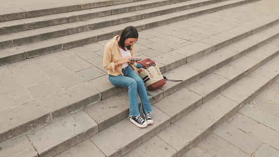 Traveler girl using looking mobile phone sitting on the steps of an old building in the historical part of an old European city, view from above