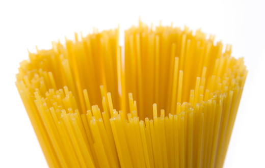 A bundle of uncooked, dry spaghetti pasta noodles, a starch staple and ingredient of Italian cuisine, against a white background.