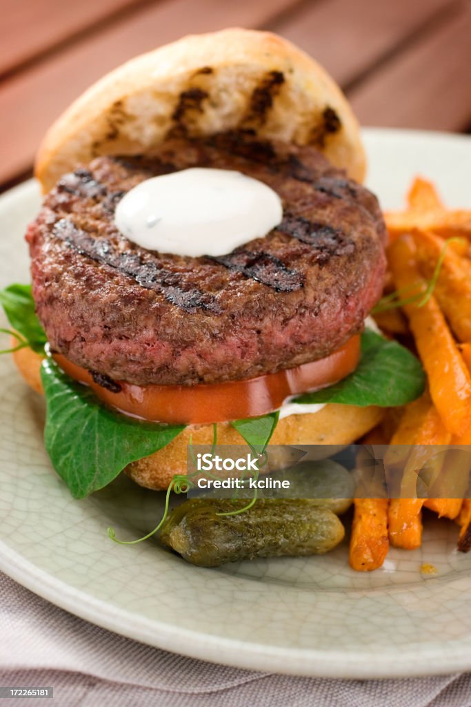 Grilled Lamb Burger "A burger of a different kind, mildly spiced ground lamb cooked to perfectly medium rare and served on a rosemary ciabatta roll with fresh pea vines and heirloom tomato slice, topped with yogurt mint mayonnaise.  Served with a side of seasoned sweet potato frites.  Shallow dof" Burger Stock Photo