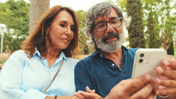 istock Retired couple talking, using mobile phone while sitting outside in the park in autumn 1722656246