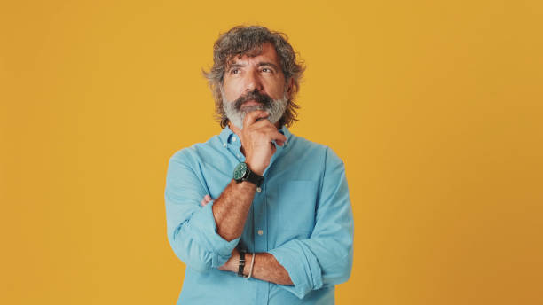 istock Elderly white-haired bearded man wears a blue shirt, makes a decision, isolated on an orange background in the studio 1722656257