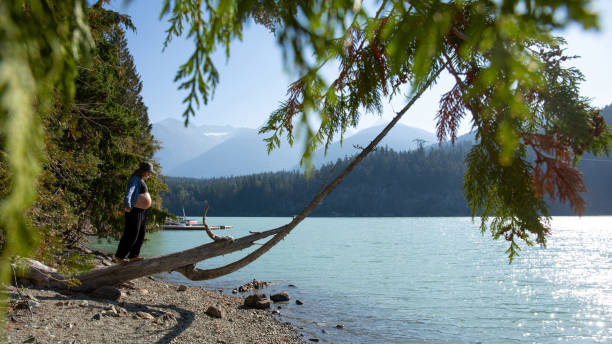 mujer joven se balancea y camina a lo largo del tronco, a la orilla del lago - stone wellbeing zen like blue fotografías e imágenes de stock