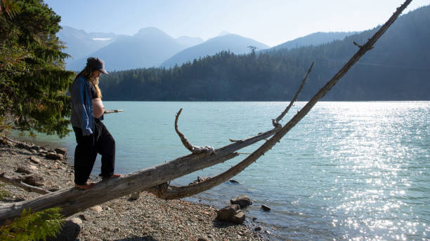 mujer joven se balancea y camina a lo largo del tronco, a la orilla del lago - stone wellbeing zen like blue fotografías e imágenes de stock