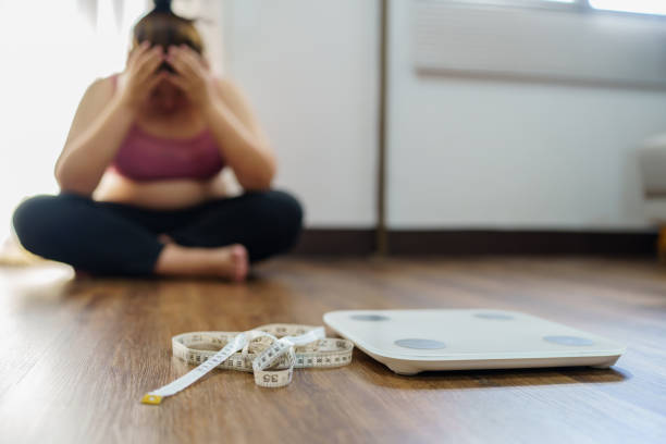 donna obesa con grasso sconvolto annoiato di dieta perdita di peso fallire dieta grassa e scala donna asiatica triste sulla scala di peso a casa controllo del peso - chilogrammo foto e immagini stock