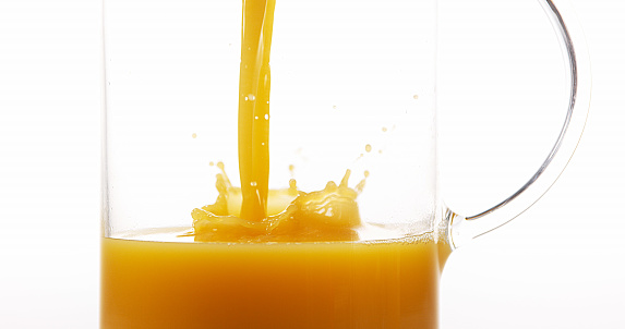 Orange Juice being poured into Glass against White Background