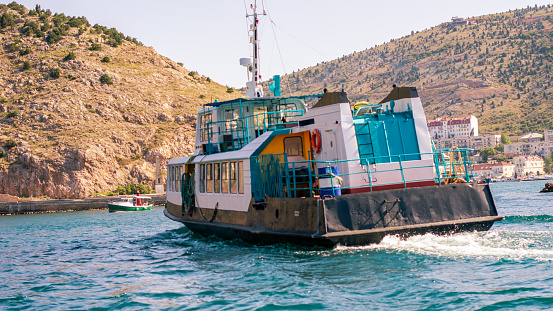 Rear view of a water taxi in a bay with yellow hills in the background on a sunny day.