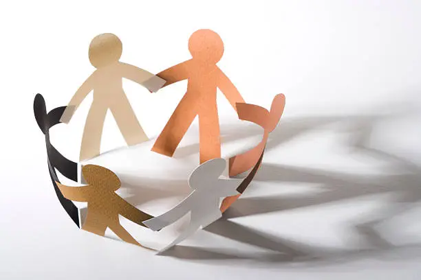 Top-down view of six diverse paper cutout people. The shadows form two heart shapes. Sharp on the front people's heads.