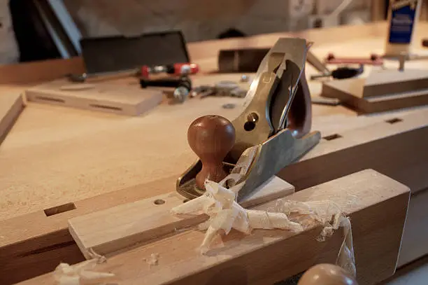 A bronze smoothing plane with wood shavings freshly cut from a piece of maple hardwood.