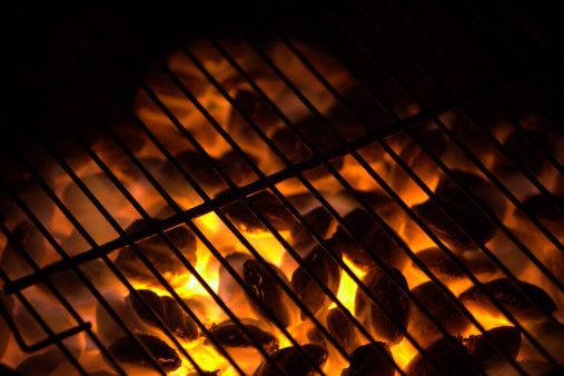 Close up view of an empty grill with wood underneath burning and fire coming out through the grill.