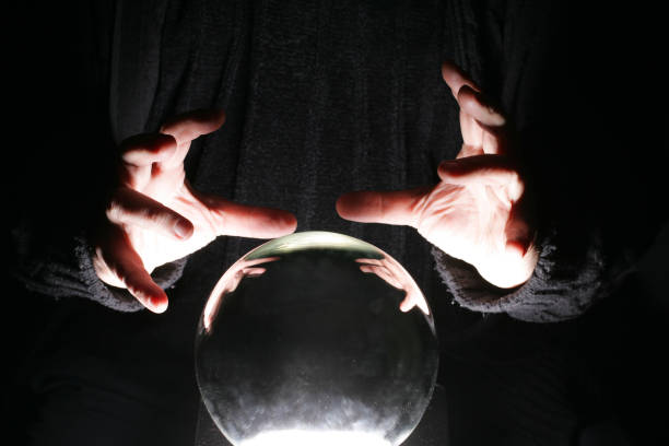 Hands of a black garbed person poised over a crystal ball stock photo
