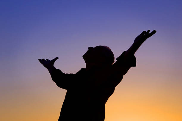 Arms Open Wide Man standing at sunset with arms open and looking to the sky. relief emotion stock pictures, royalty-free photos & images
