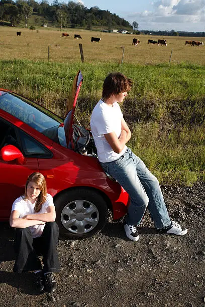 Unhappy teenagers with a broken down car on a country road