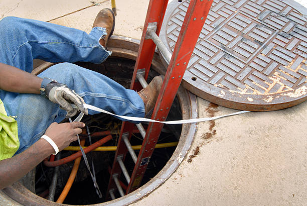 City Utility Worker "Waist down view of urban worker making repairs in manhole under city street during the day. Work clothing includes fluorescent vest, protective work gloves and work boots." manhole stock pictures, royalty-free photos & images