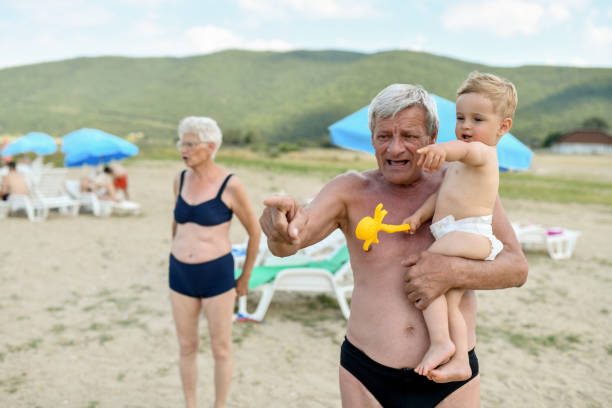 bebé niño reconociendo formas en el agua señalado por el abuelo en la playa - grandson water waterfront portrait fotografías e imágenes de stock