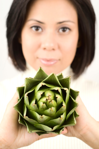 Asian woman confidently displays an artichoke.