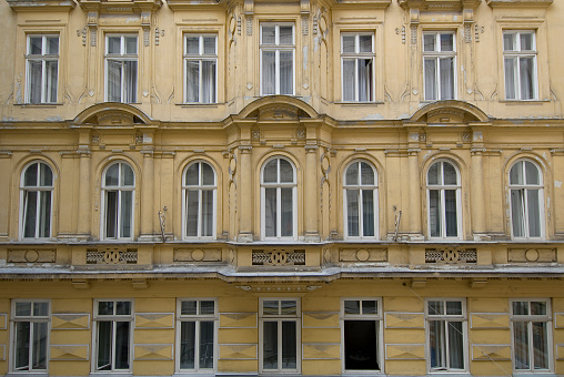 Old building in a city street. The empty house with the weathered exterior is located between other buildings. The facade is bright and the paint is peeling off. Renovation is very expensive.