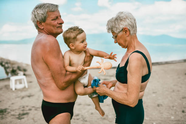 조부모가 해변에서 옷을 입히려고 하는 동안 고군분투하는 아기 - grandson water waterfront portrait 뉴스 사진 이미지