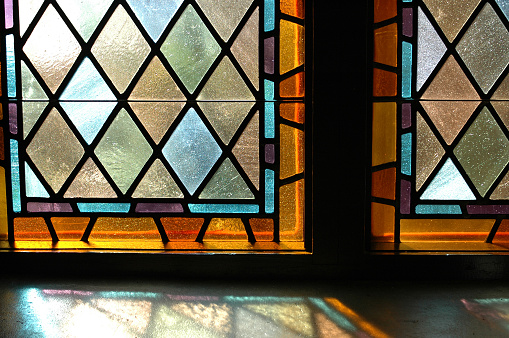 Colorful stained glass filters sunlight as it falls upon the chapel window sill.
