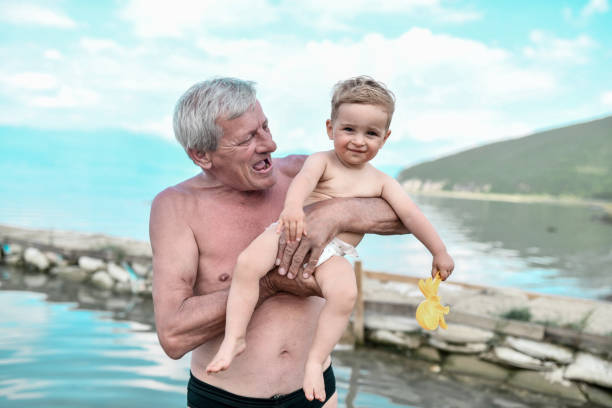 해변에서 어린 손자와 함께 휴식을 취하는 동안 할아버지가 보여주는 행복과 흥분 - grandson water waterfront portrait 뉴스 사진 이미지