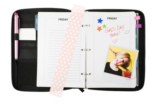 Black agenda open on Friday with pink bookmark and funny picture. White background.