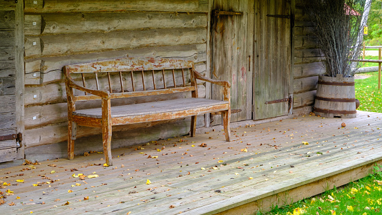 A very old wooden barn in front with an old wooden bench. An authentic example of a Latvian farm building.