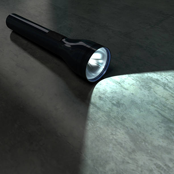 Black flashlight illuminating part of a dark metallic floor stock photo