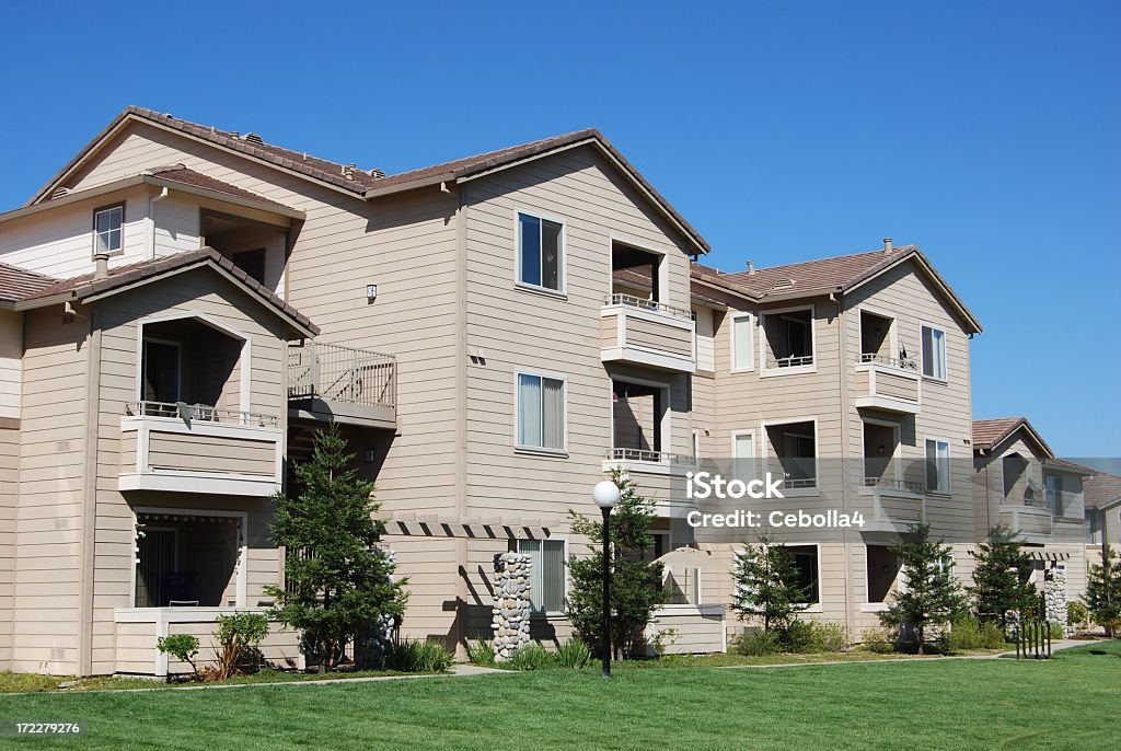 Apartment Complex Living Suburbs in California. Green grass in the foreground, blue sky in the background. A few trees scattered between buildings. Manicured lawn. Well-kept buildings, freshly painted. Apartment Stock Photo