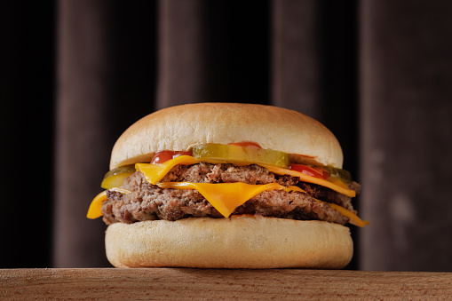 perfect tasty double cheeseburger on wooden table on brown background, bottom view