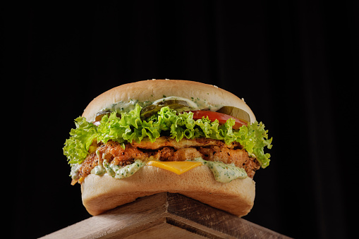 perfect tasty big chicken cheeseburger on wooden table on brown background