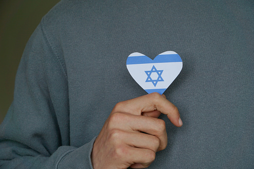 A child clutches an Israel flag shaped as a heart against their chest, symbolizing love and connection.