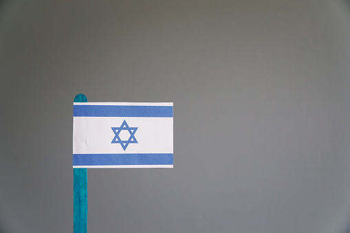 Israeli flag waving proudly against a neutral gray backdrop, symbolizing the nation's identity and unity.