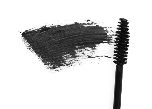 Applicator and black mascara smear on white background, top view