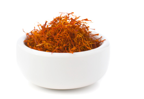 Saffron, an aromatic herb spice seasoning often used in Spanish, southern European and Middle Eastern cuisine. The dried food plant strands are piled and heaped in a white ceramic bowl. Isolated on white.