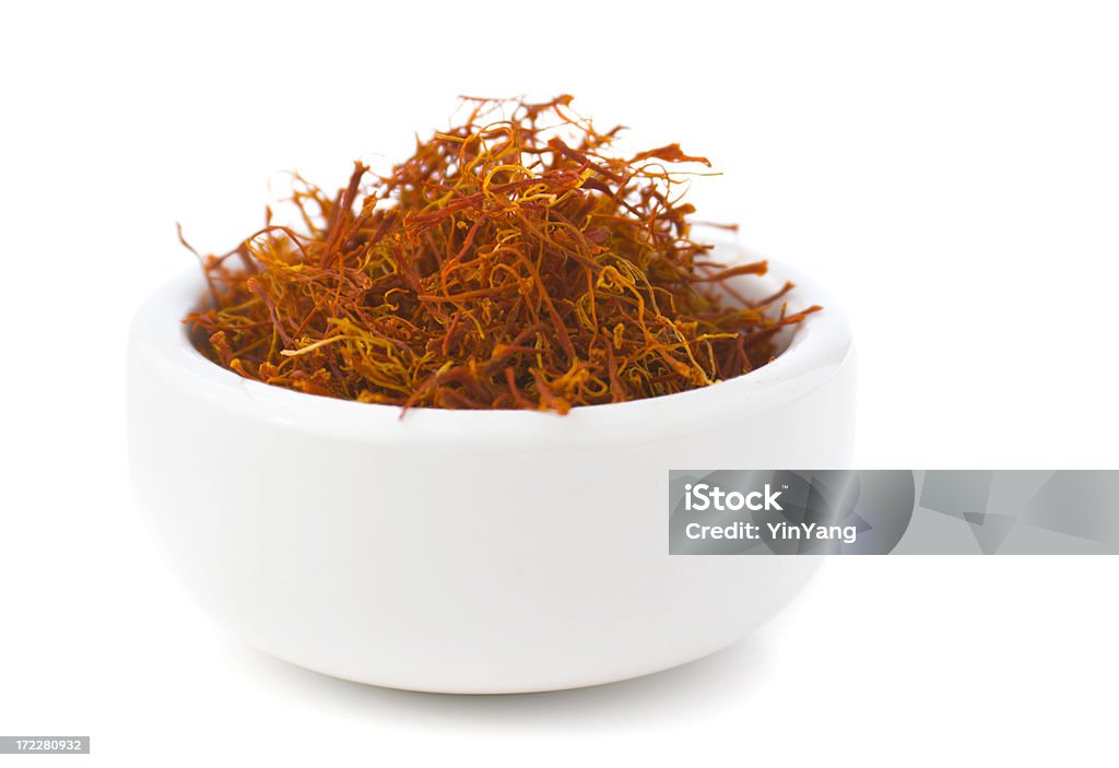 Saffron Spice in Bowl, Red Spanish Seasoning Isolated on White Saffron, an aromatic herb spice seasoning often used in Spanish, southern European and Middle Eastern cuisine. The dried food plant strands are piled and heaped in a white ceramic bowl. Isolated on white. Saffron Stock Photo