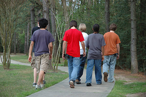 A group of six teenage boys walking away from the camera on a winding sidewalk through a wooded area on a beautiful spring day.