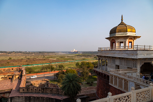 The Red Fort in Agra, is a UNESCO World Heritage site renowned for its rich history and Mughal architecture. Constructed primarily of red sandstone, the fort stands as a testament to the opulence and military might of the Mughal Empire. One of the fort's most captivating features is its vantage points offering distant views of the Taj Mahal. The frame captures this unique relationship between the two iconic structures, allowing a glimpse of the Taj Mahal in the background, linking two of India's most significant landmarks in a single image.