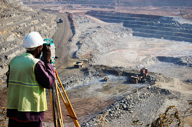 Surveying the Pit 2 "A locally employed surveyor at an open-pit copper mine in Zambia.  He peers through his survey instrument to record the daily changes in the open-pit, and help guide mining activities to the engineer's plans." drill photos stock pictures, royalty-free photos & images