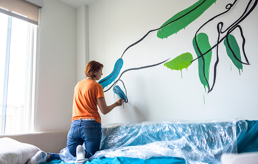 Mature Caucasian redhead woman, interior designer craft colorful whale mural. Living room decor