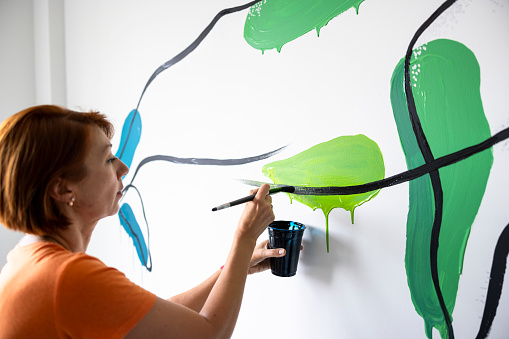 Wall transformed into canvas: mature Caucasian female interior designer drawing whale mural in bright room