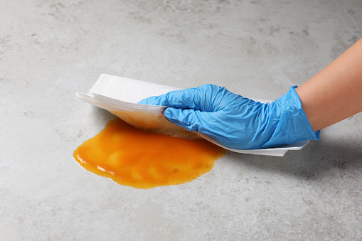 Woman wiping spilled sauce with paper towel on grey surface, closeup