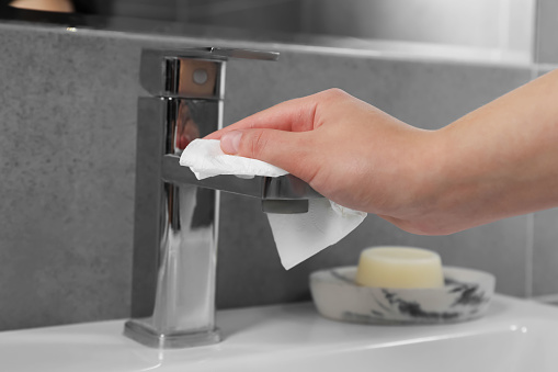 Woman cleaning faucet of bathroom sink with paper towel, closeup