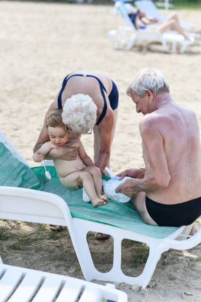 해변에서 아기의 기저귀를 제거하는 조부모 - grandson water waterfront portrait 뉴스 사진 이미지