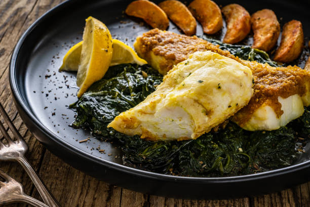 istock Seared cod fillet on cooked spinach with baked potatoes on wooden background 1722832955